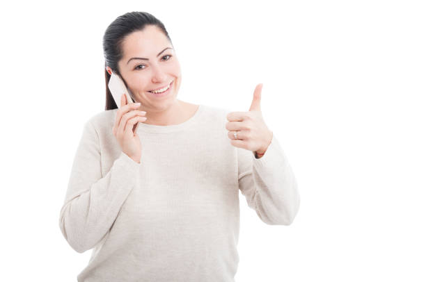 Beautiful happy woman showing thumb up gesture while talking on cellphone on white background