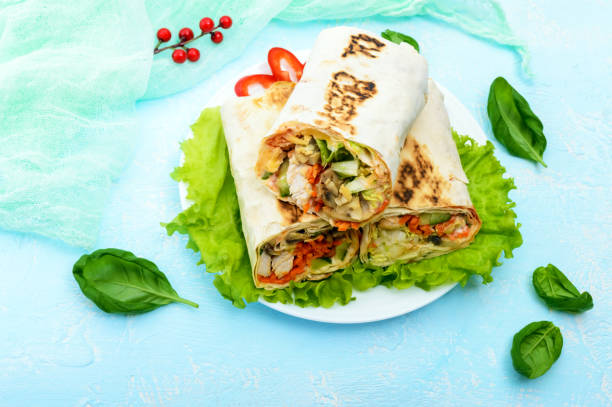 istock Shawarma - Middle Eastern dish made from lavash (pita), stuffed with chicken, mushrooms, fresh vegetable salad, sauce. Serving on lettuce leaves on a light background. The top view. 654112894