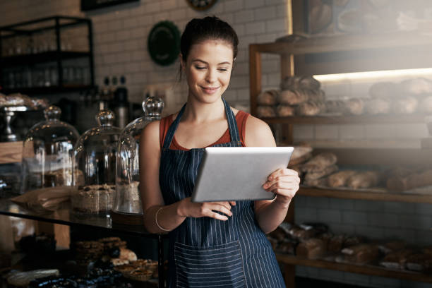 I have everything you need on your tea break Shot of a young woman using a digital tablet while working in a coffee shop cafe tablet stock pictures, royalty-free photos & images