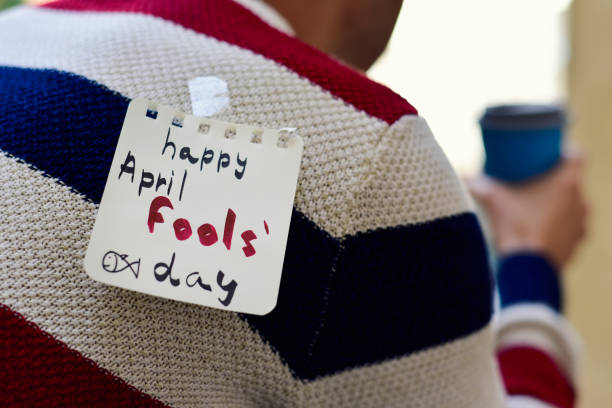 young man and text happy april fools day closeup of a young caucasian man seen from behind having a coffee, with a note with the text happy april fools day attached with tape to his back april fools day stock pictures, royalty-free photos & images