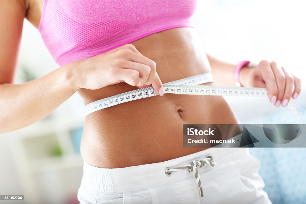 Slim young woman measuring her waist with a tape measure Midsection of young woman measuring her fit waist Dieting Stock Photo