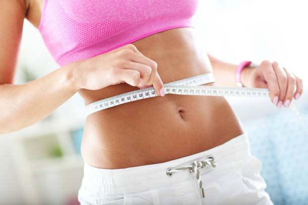 slim young woman measuring her waist with a tape measure - waist imagens e fotografias de stock