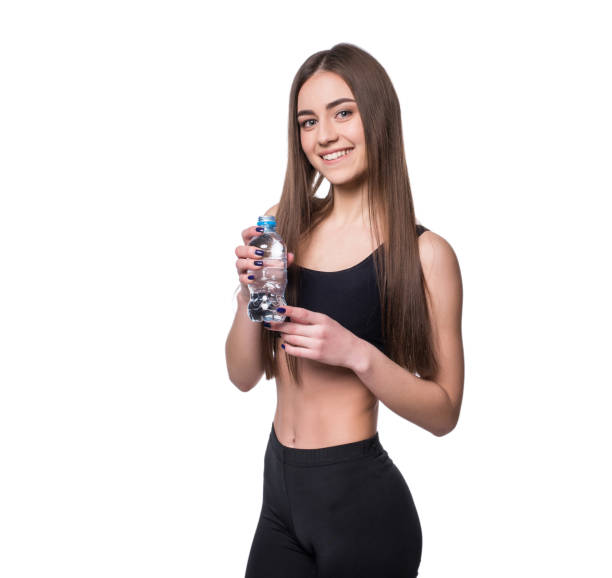 modèle positif femme fitness après entraînement tenant une bouteille d’eau pure sur fond blanc. - aerobics beautiful bottle body photos et images de collection