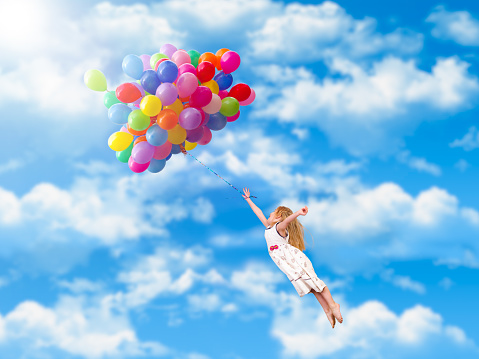 Child flies on the balloons. Blue sky, clouds. A little girl in a white dress