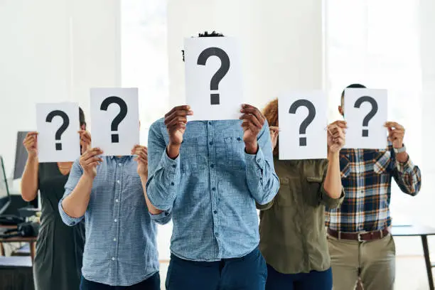 Shot of a group of businesspeople holding questions marks in front of their faces