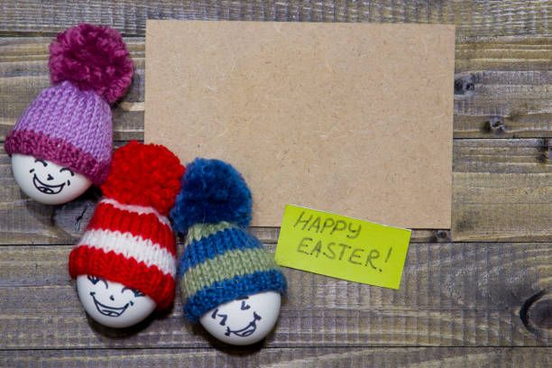 oeufs de pâques sur le bois. émoticônes dans un bonnet tricoté avec pompons. à la main. - easter bonnets photos photos et images de collection