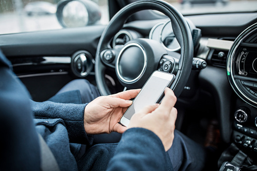 Man sitting in car using mobile phone while driving, focus on hands.