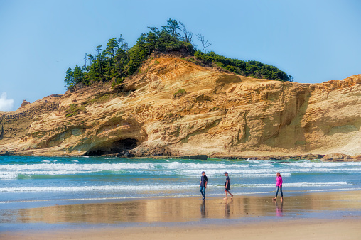 Two boys and a girl walk the edge of the surf on a sunny day at Cape Kiwanda in Pacific City on the Oregon Coast.