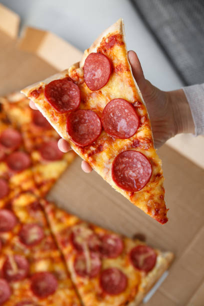 istock Pepperoni or salami pizza. Hand holding a piece. 654289000