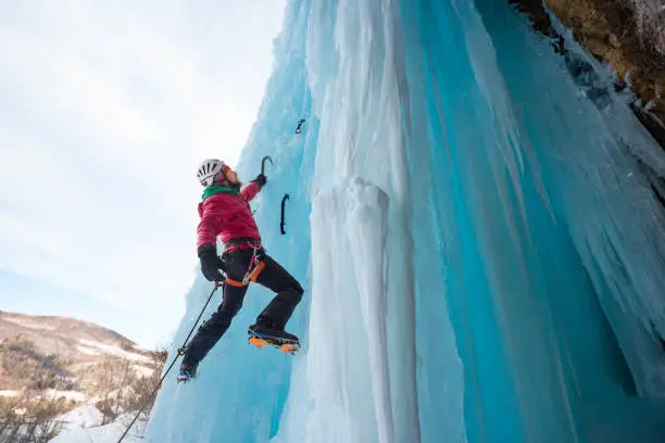 Caucasian adult male alpinist ice climbing outdoor in nature on frozen waterfall