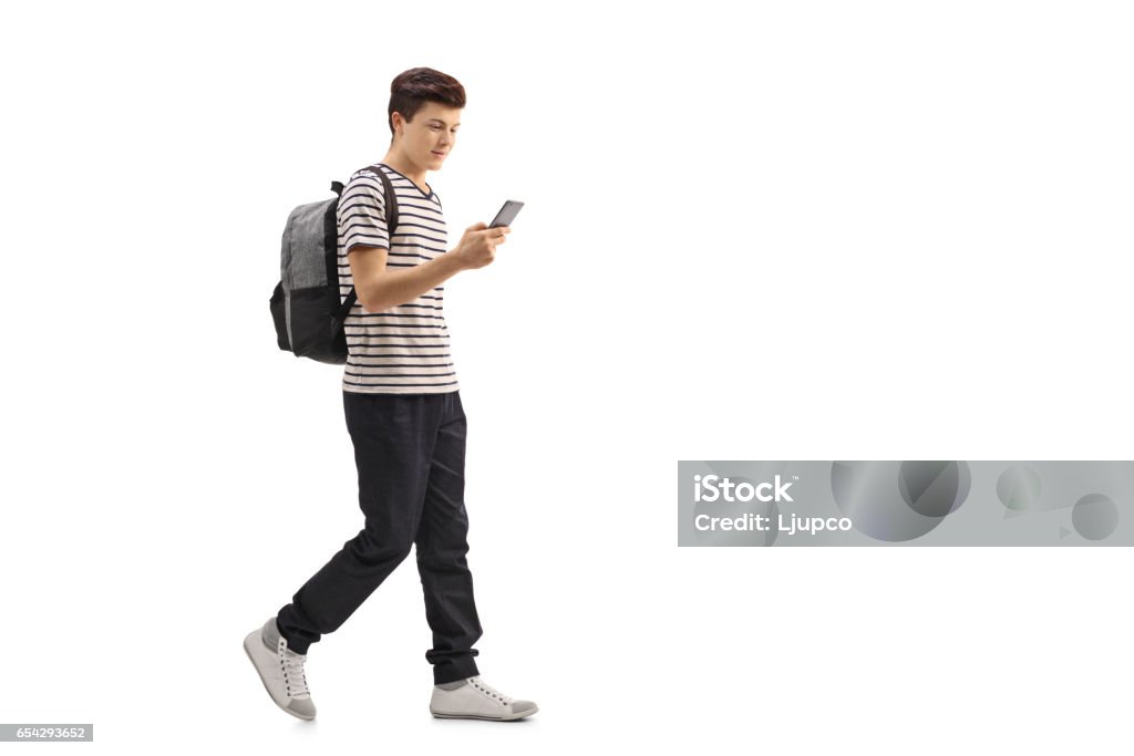 Teenage student walking and looking at a phone Full length profile shot of a teenage student walking and looking at a phone isolated on white background Teenager Stock Photo