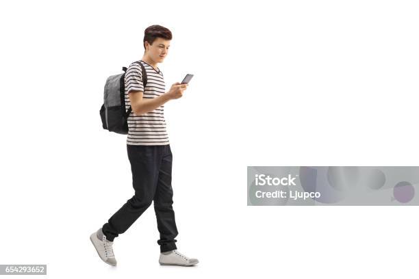 Teenage Student Walking And Looking At A Phone Stock Photo - Download Image Now - Teenager, Adolescence, Walking