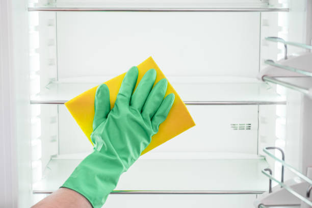 istock Man's hand in green rubber protective gloves cleaning empty refrigerator 654297160