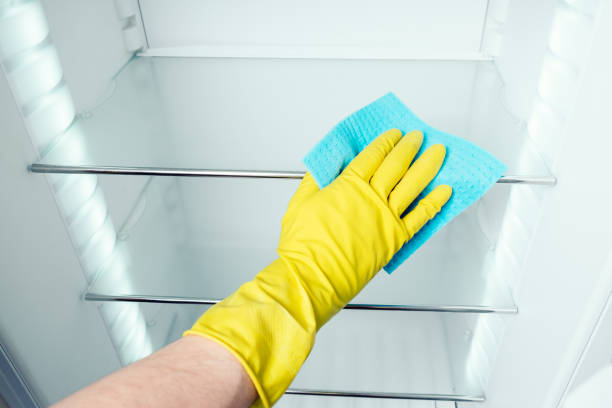 istock Man's hand in gloves cleaning white fridge with blue rag at kitchen 654297168