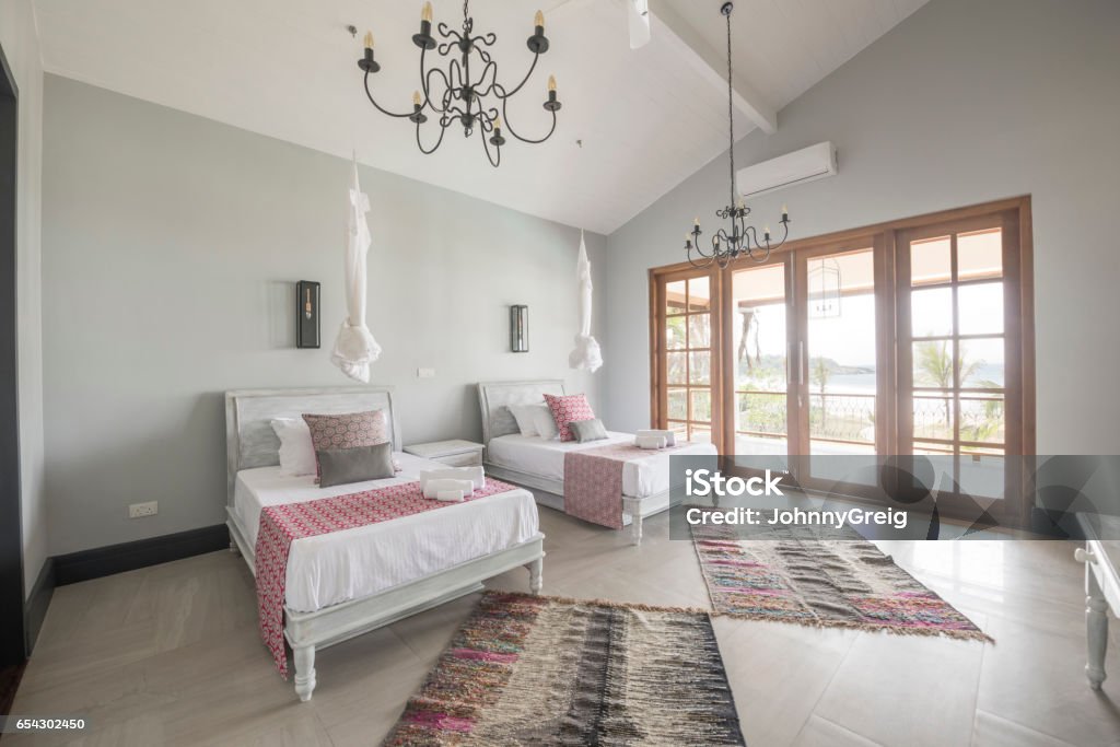 Twin beds in contemporary apartment room Modern hotel room with two beds and french doors with natural light, ethnic floor covering on tiled floor Twin Bed Stock Photo
