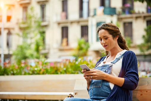 Pregnant woman text messaging while sitting on bench