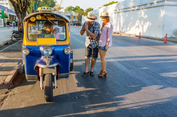 Happy mature couple respectfully paying after using a tuk tuk for transport outside the Royal Palace in Bangkok Thailand