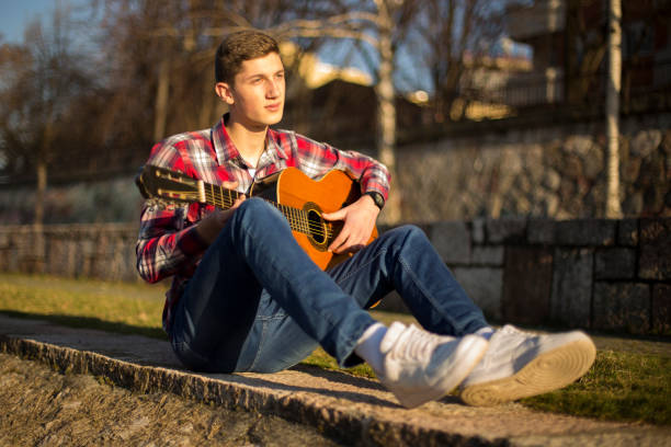 istock Young boy playing acoustic guitar by the city river 654446284