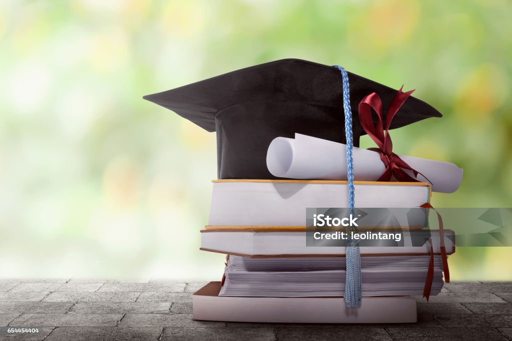 Graduation hat with degree paper on a stack of book Graduation hat with degree paper on a stack of book against blurred background University Stock Photo