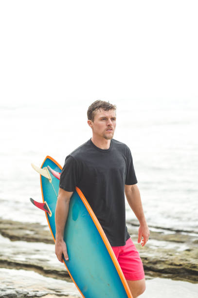 istock Young mid-20s man carrying surfboard on Hawaii beach 654518196