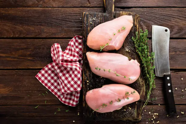 Photo of Raw chicken breasts fillets with thyme and spices on wooden cutting board on rustic background, copy space, directly above