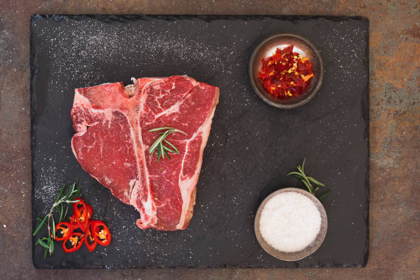 Raw fresh meat T-bone steak and seasoning Raw T-bone steak with salt and rosemary. Top view, blank space porterhouse steak stock pictures, royalty-free photos & images
