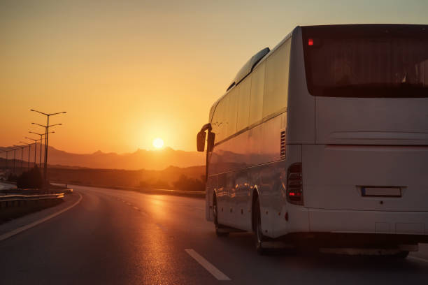 istock White bus driving on road towards the setting sun 654563032