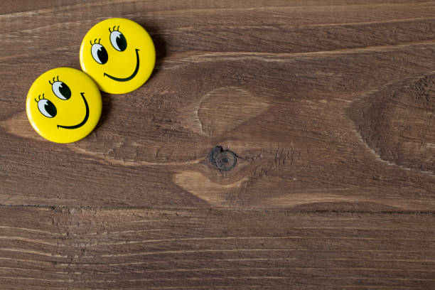 istock Two yellow buttons with smiley faces on a wooden background 654658562