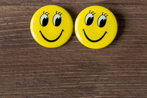 istock Two yellow buttons with smiley faces on a wooden background. Close up 654658742
