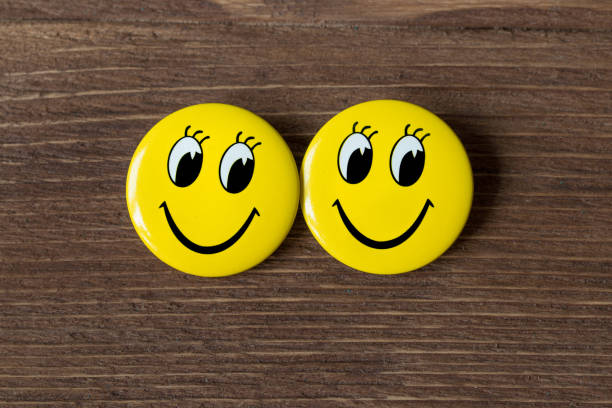 istock Two yellow buttons with smiley faces on a wooden background. Top view 654658896