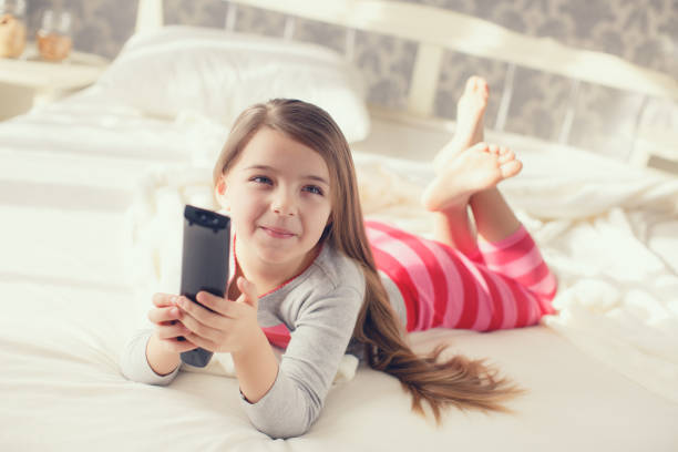 istock Little girl lying in bed with a remote control TV 654689290
