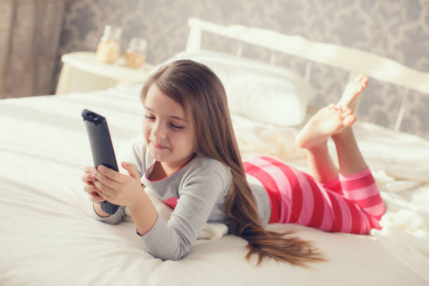 istock Little girl lying in bed with a remote control TV 654689306