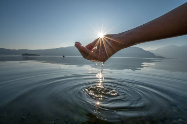 Human hand cupped to catch fresh water from lake. Shot in Italy at the lake Maggiore, beautiful sunset, sunbeam reflections on the water surface. Environment concept idea.