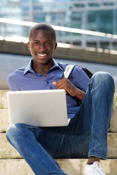 istock Happy young african man sitting outdoors with laptop 654703572