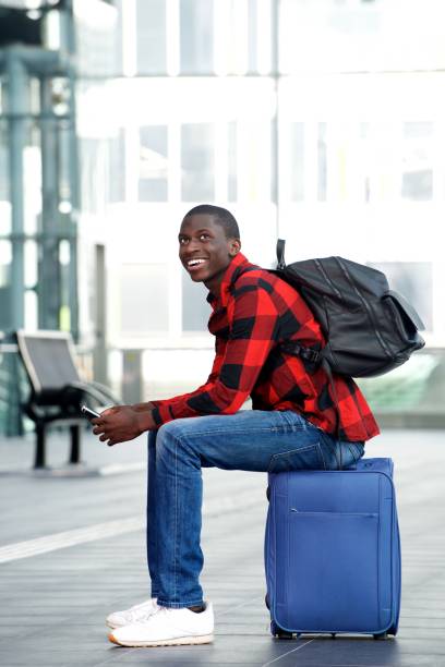 istock Smiling young man sitting on traveling bag with mobile phone 654703792