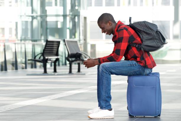 istock Young man sitting on traveling bag and using cell phone 654703808