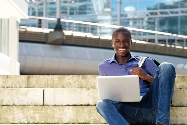 istock Happy young student sitting on steps with laptop 654703838