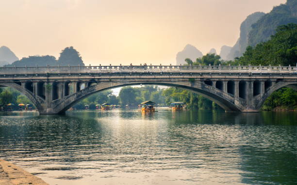 bateaux avec des touristes flottant sur la rivière li, au-dessous d’un pont de pierre au coucher du soleil - yangshuo photos et images de collection