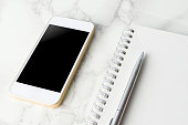 Blank smart phone screen with blank notebook on marble desk