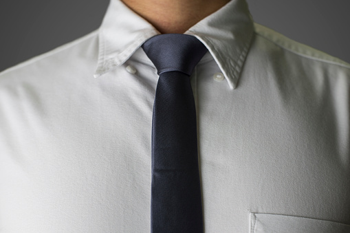 Close up on a man in white shirt and grey necktie on a grey background