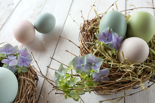 Easter nest with colorful eggs and tender blossoms in vintage style on a white wooden table
