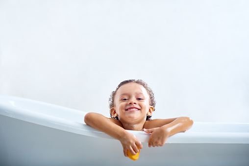 Pretty little girl sitting in bathtub and leaning on the edge