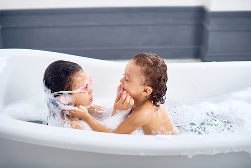 Two cute sisters touching faces of each other when they taking a bath
