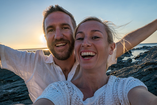 Young couple taking selfie portrait by the sea at sunset. Shot in Cape Town, South Africa.