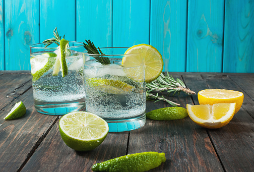 Alcoholic drink gin tonic cocktail with lemon, rosemary and ice on rustic wooden table