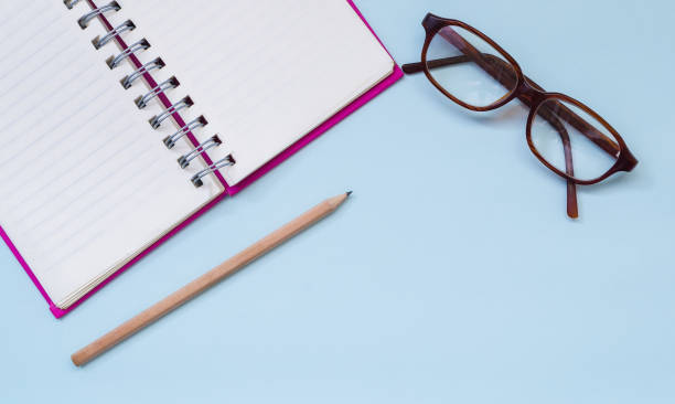istock Eyeglasses , pencil and blank notebook on blue background from top viewpoint 654918252