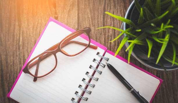 istock Glasses, pen and opened notebook on wooden table with flowerpot from top view point 654925504