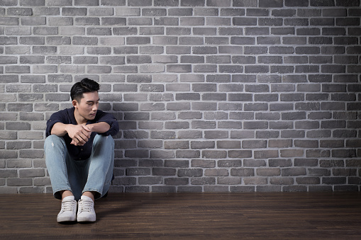 man sit and feel depressed with brick wall ,asian