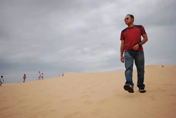 Asian Man walking on a desert sand dune in Vietnam, Muine.