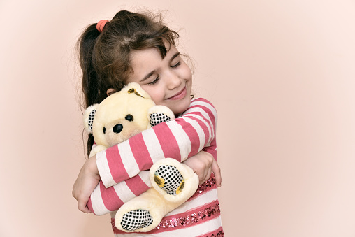 Smiling young girl with closed eyes hugging and playing with teddy bear